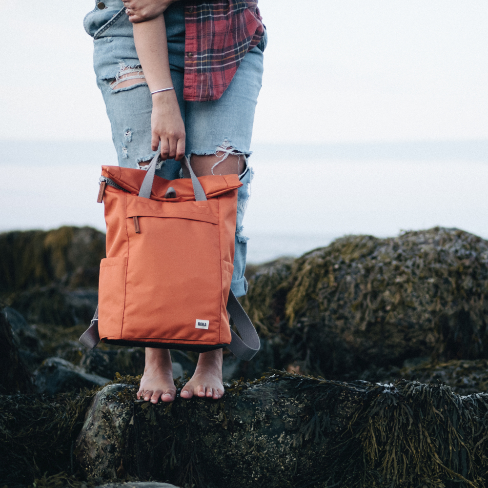 finchley sustainable medium backpack atomic orange on the beach by roka